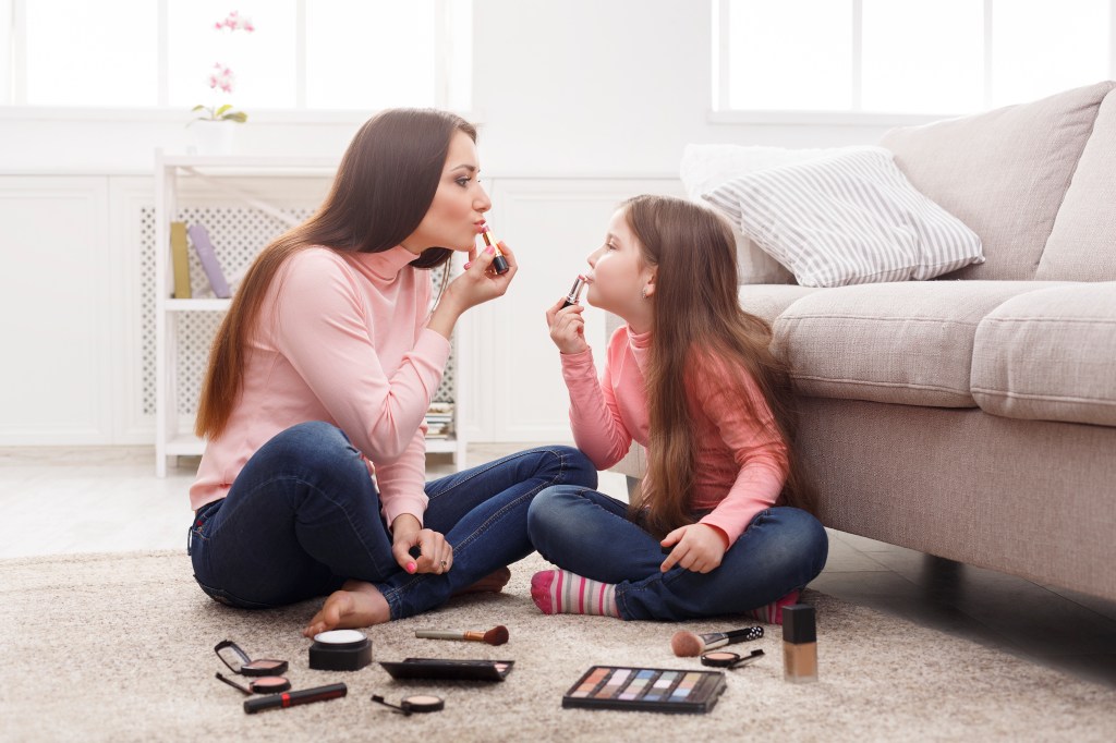 Mother and daughter sitting on the floor in the bedroom, bonding by doing makeup together